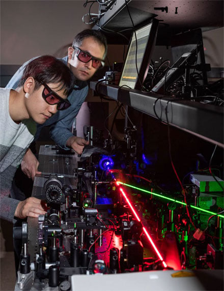 Georgia Tech researchers Kyu-Tae Lee and Mohammad Taghinejad demonstrate frequency doubling on a slab of titanium dioxide using a red laser to create nonlinear effects with tiny triangles of gold. The blue beam shows the frequency-doubled light and the green beam controls the hot-electron migration. Courtesy of Rob Felt, Georgia Tech.