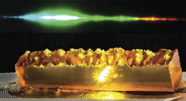  Figure 1. A visible supercontinuum produced by a 1-mm-long crystal of OPGaP pumped by 30-nJ femtosecond pulses from a 100-MHz, 1040-nm Yb-doped fiber laser. The crystal’s characteristic yellow color of GaP can be seen. The domain structure in OPGaP is grown by vapor-phase epitaxy from a patterned GaP substrate (the bottom surface of the crystal) and terminates with a rough upper surface. Green light corresponding to the second harmonic of the pump laser wavelength dominates the supercontinuum and serves as a pump for parametric gain processes that generate the other colors. Courtesy of Derryck T. Reid, Marius Rutkauskas, and Luke Maidment. 