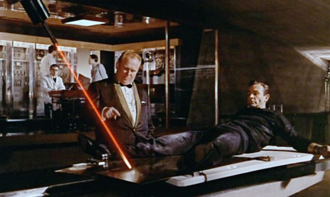 Auric Goldfinger (Gert Frobe, left) looks on as James Bond (Sean Connery, right) stares down an industrial cutting laser. Courtesy of MGM/UA.