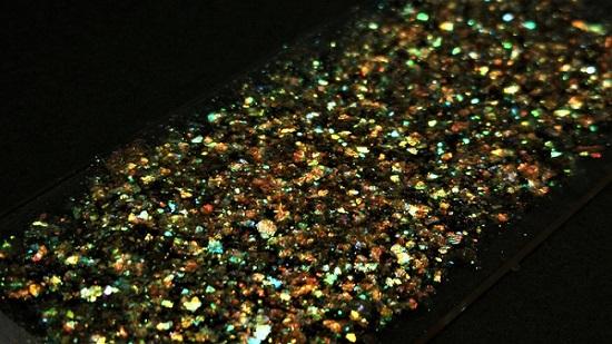 A close-up photograph of a glass slide that has been covered with gold flakes with high lighting contrast and observed at a larger angle. Courtesy of Benjamin Droguet. 