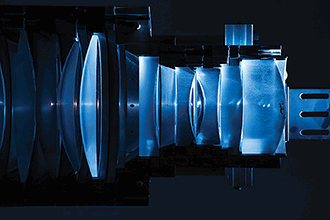 A cutaway lithography lens lit with flashes and green lasers is on display at the University of Rochester.