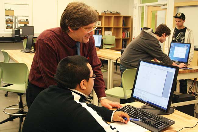 Jacob Longacre, an assistant professor and leader of the photonics program at Quinsigamond Community College in Massachusetts, works with students in an electronics class on troubleshooting amplifier and power supply circuits. 