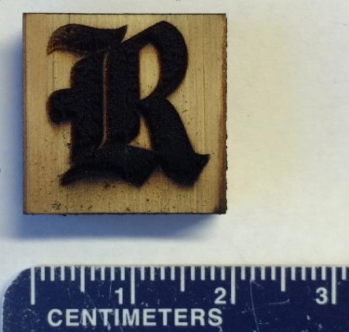 Rice University athletics logo made from laser-induced graphene on a block of pine. Rice University.
