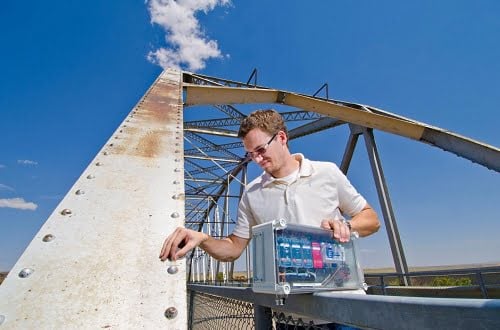Sandia National Laboratories mechanical engineer Stephen Neidigk positions a Comparative Vacuum Monitoring sensor on a bridge. In his other hand is the control system that periodically checks the sensor and a wireless transmitting device to autonomously alert the maintenance engineers if it detects a crack. 