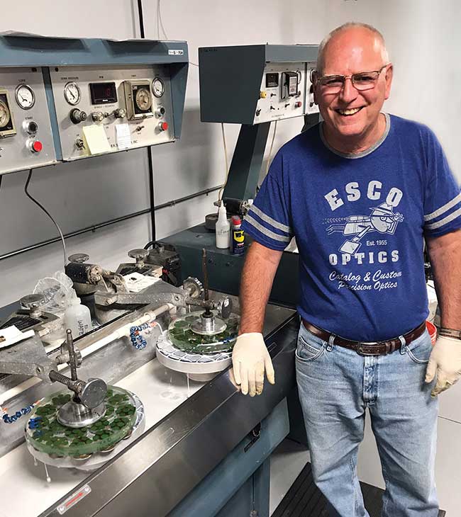 Esco Optics’ Bruce Van Orden, who has been with the company for 43 years, stands with a precision spindle polishing machine.