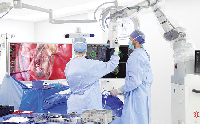 Surgeons use Synaptive Medical’s Modus V to perform a neurosurgery. Preoperative imaging is displayed on the right, while a real-time image is displayed on a monitor to the left. Courtesy of Synaptive Medical. 