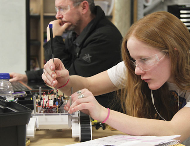 A Northwestern Michigan College student troubleshoots a wheeled robot that she programmed in Python language.