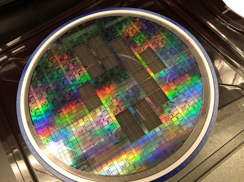 A 300 mm semiconductor wafer fabricated by AIM Photonics using a low-optical-loss passive fabrication technique and components developed by the U.S. Naval Research Laboratory. The PIC semiconductor wafer is patterned into 64 identical parts, each one called a reticle, approximately 1 in. by 1 in., 20 reticles have been removed from the wafer for analysis. Courtesy of U.S. Naval Research Laboratory Optical Sciences Division.
