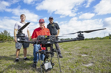 From left: FAU graduate student Anthony Davis; Warner Miller; and collaborator Pedram Nimreezi, stand behind the large drone, which includes a network of a ground station, lasers, and fiber optics. (Courtesy of Alex Dolce via FAU).