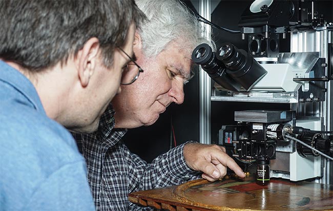 William Brown (right), former chief conservator of the Art Conservation Center at the North Carolina Museum of Art (NCMA), and Martin Fischer, associate research professor of chemistry and physics at Duke University, study the painting ‘St. John the Evangelist Reproving the Philosopher Crato’ by Francescuccio di Cecco Ghissi (1375), a gift from the Samuel H. Kress Foundation. In the study, pump-probe microscopy investigates early signs of vermilion degradation, in which the red pigment gradually darkens and turns gray. See Reference 4. Courtesy of Simone Degan/Duke University.