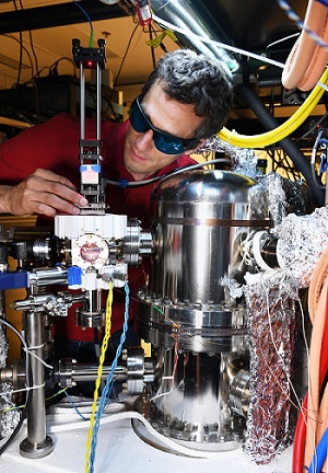 NIST scientist Stephen Eckel behind a pCAVS unit (silver-colored cube left of center) that is connected to a vacuum chamber (cylinder at right). Courtesy of C. Suplee, NIST.
