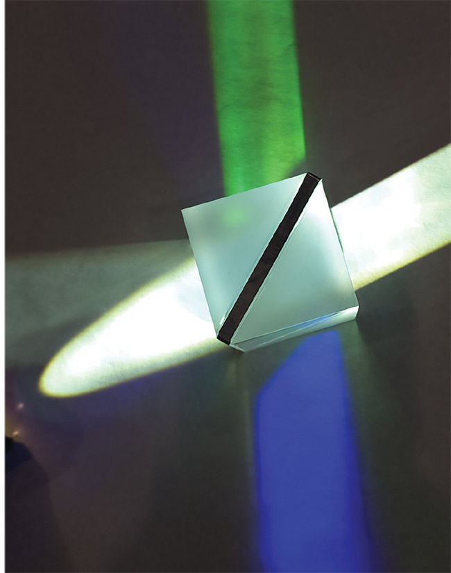 A high-dispersion grating prism, or grism. The dark diagonal line is the grating, and the white triangular structures are the prisms. White light enters the grism at an angle from the left and exits on the right. Blue light is separated from the incoming light and exits from the bottom. The green beam results from the imaging of the grating. Courtesy of Wasatch Photonics.