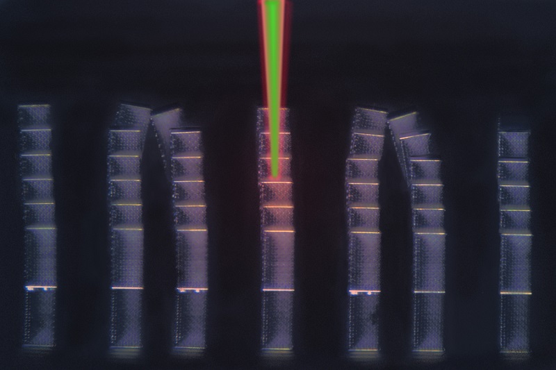 This optical micrograph shows an array of microscopic metamaterial samples on a reflective substrate. Laser pulses have been digitally added, depicting pump (red) and probe (green) pulses diagnosing a sample in the center. The LIRAS technique sweeps through all samples on the substrate within minutes. Courtesy of MIT.
