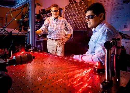 As a red beam of light is reflected in an arch, Prasad Iyer, right, and Igal Brener demonstrate optical hardware used for beam steering experiments at Sandia National Laboratories’ Center for Integrated Nanotechnologies. Courtesy of Craig Fritz.