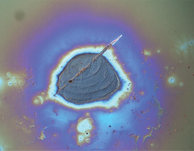 High-power laser systems are increasingly susceptible to laser-induced damage, such as the damage on a glass surface, captured here using differential interference contrast microscopy. Courtesy of Edmund Optics.