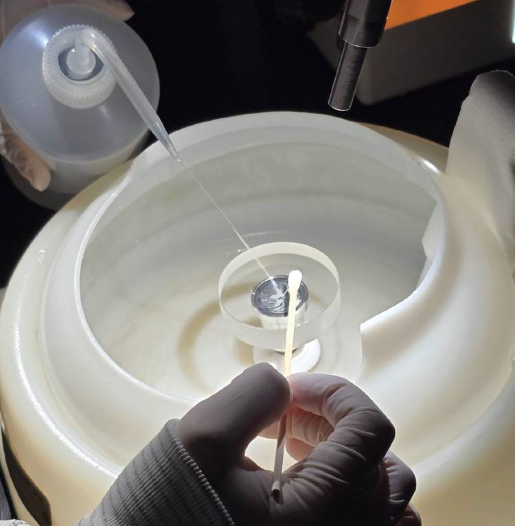 Spin cleaning, a semiautomated process, begins by spinning the optic slowly. The speed is eventually increased, and a high-purity solvent is applied a few drops at a time. Centrifugal force spreads the solvent and separates loose contamination from the optic. Courtesy of Perkins Precision Developments.