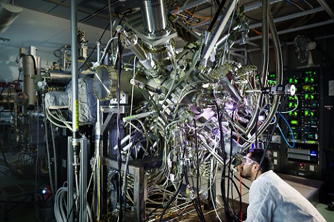 Sadhvikas Addamane, a materials scientist at Sandia National Laboratories, looking into a viewport of a molecular beam epitaxy reactor, a system Sandia will use to build experimental photonic cooling plates designed at startup Maxwell Labs for testing. Courtesy of Sandia National Laboratories/Craig Fritz.