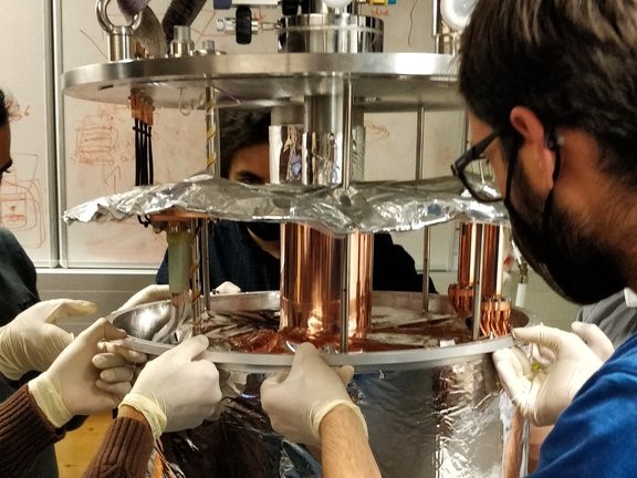 Researchers assemble a large cryostat in an experimental physics laboratory, preparing for ultra-low temperature experiments with quantum dots (QDs) on a semiconductor chip. Courtesy of the University of Innsbruck.